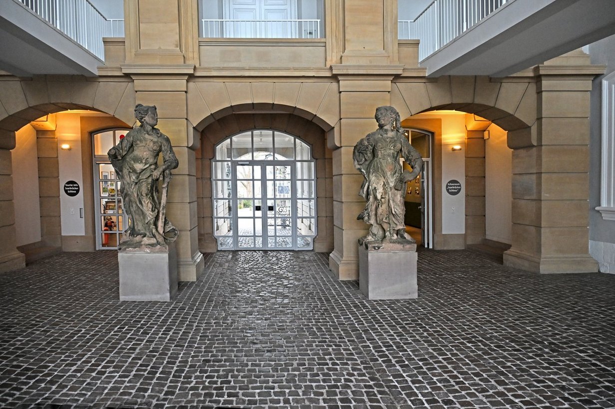 Blick auf zwei braune, leicht verwitterte weibliche Steinskulpturen im Mittelrisalit des Saarbrücker Schlosses.