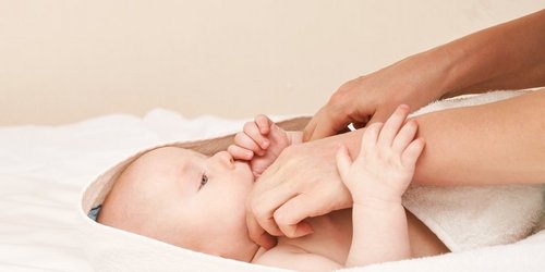 Blick von der Seite auf ein Neugeborenes welches nach einer Frauenhand greift - heller Hintergrund und helles Handtuch 